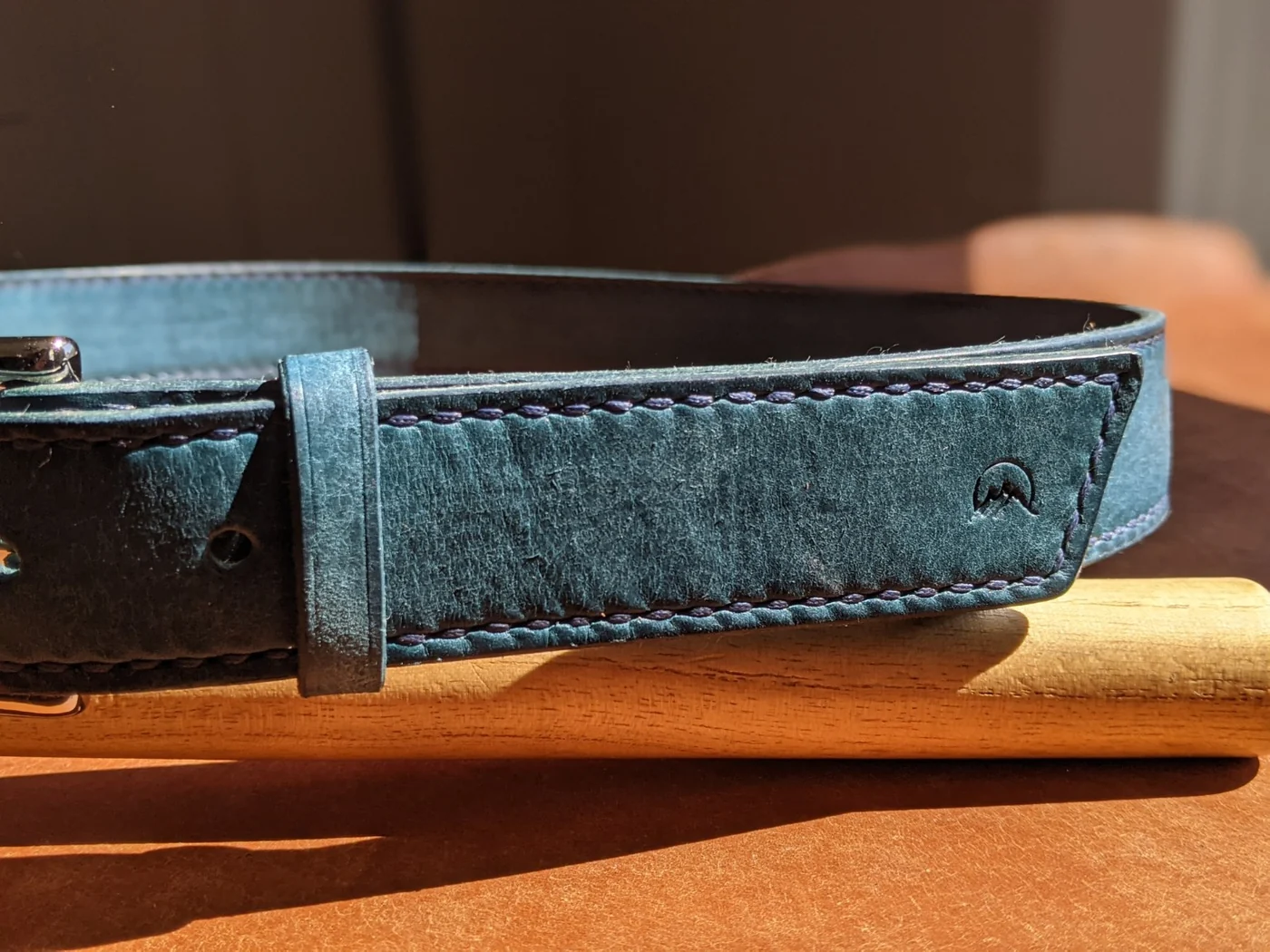 Close detail of a blue leather Moonlight Leatherworks belt showing stitching and maker mark