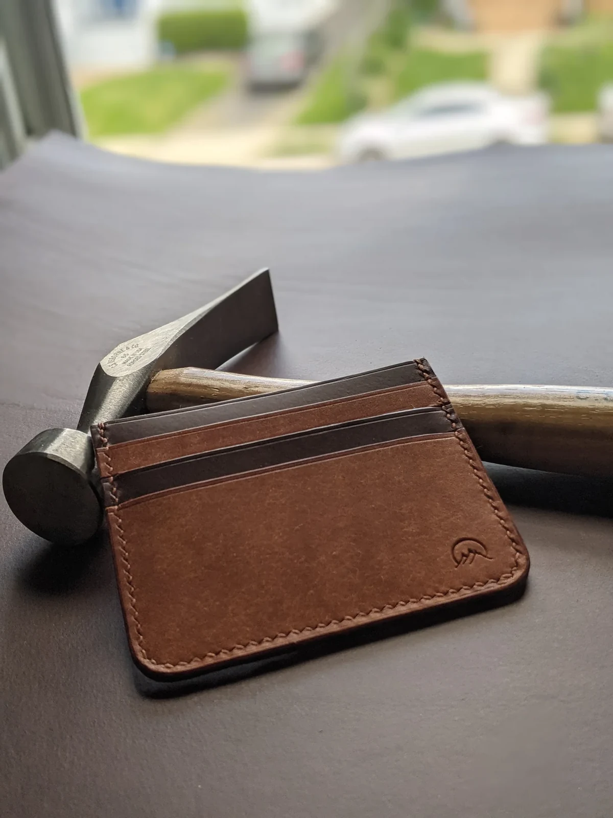 Handmade Moonlight Leatherworks Jeffrey minimalist wallet laid horizontally beside a leatherworking hammer