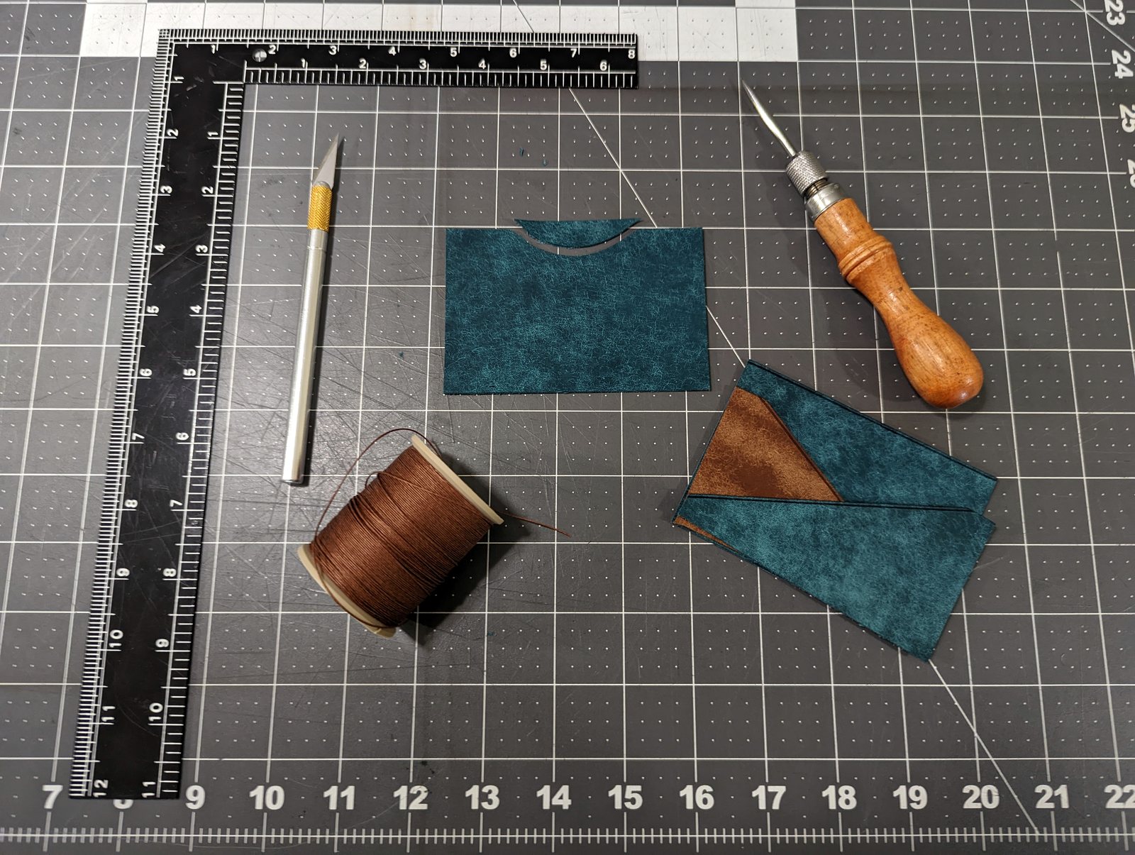 Leather pieces, hand tools, and a cutting mat on the Moonlight Leatherworks workbench