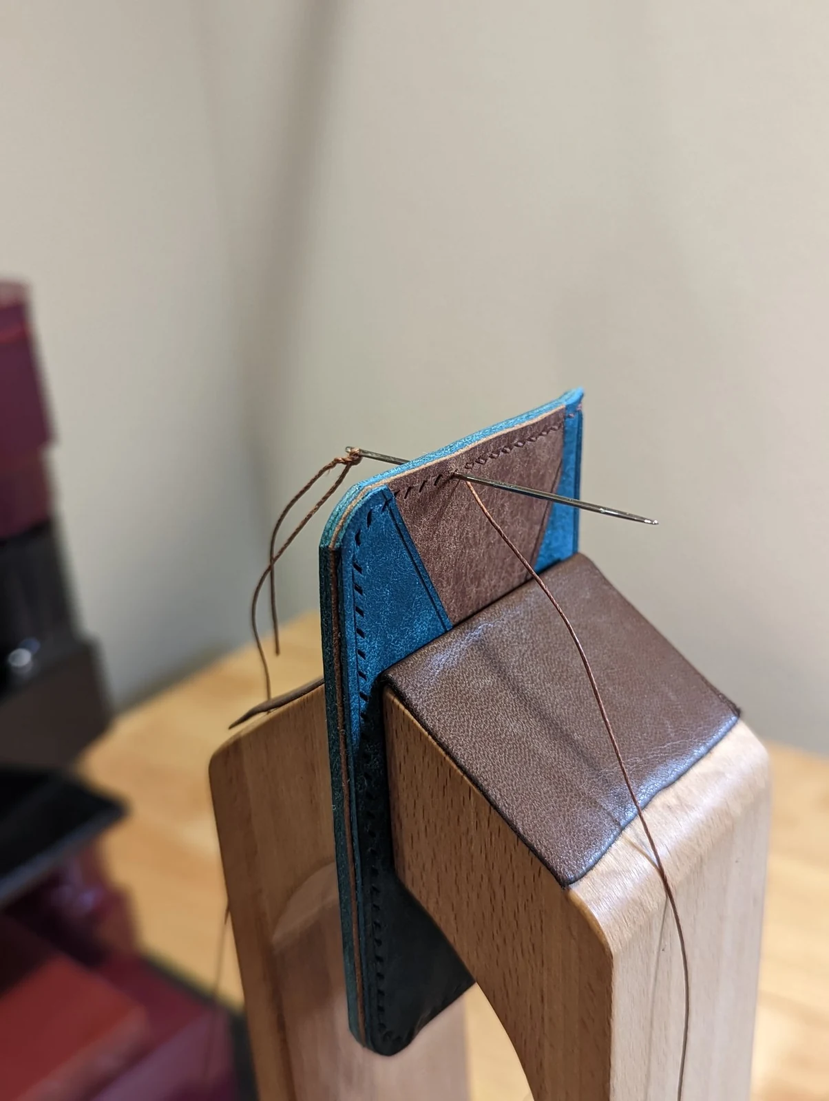 Wallet held in a stitching pony with two needles and thread passing through the leather